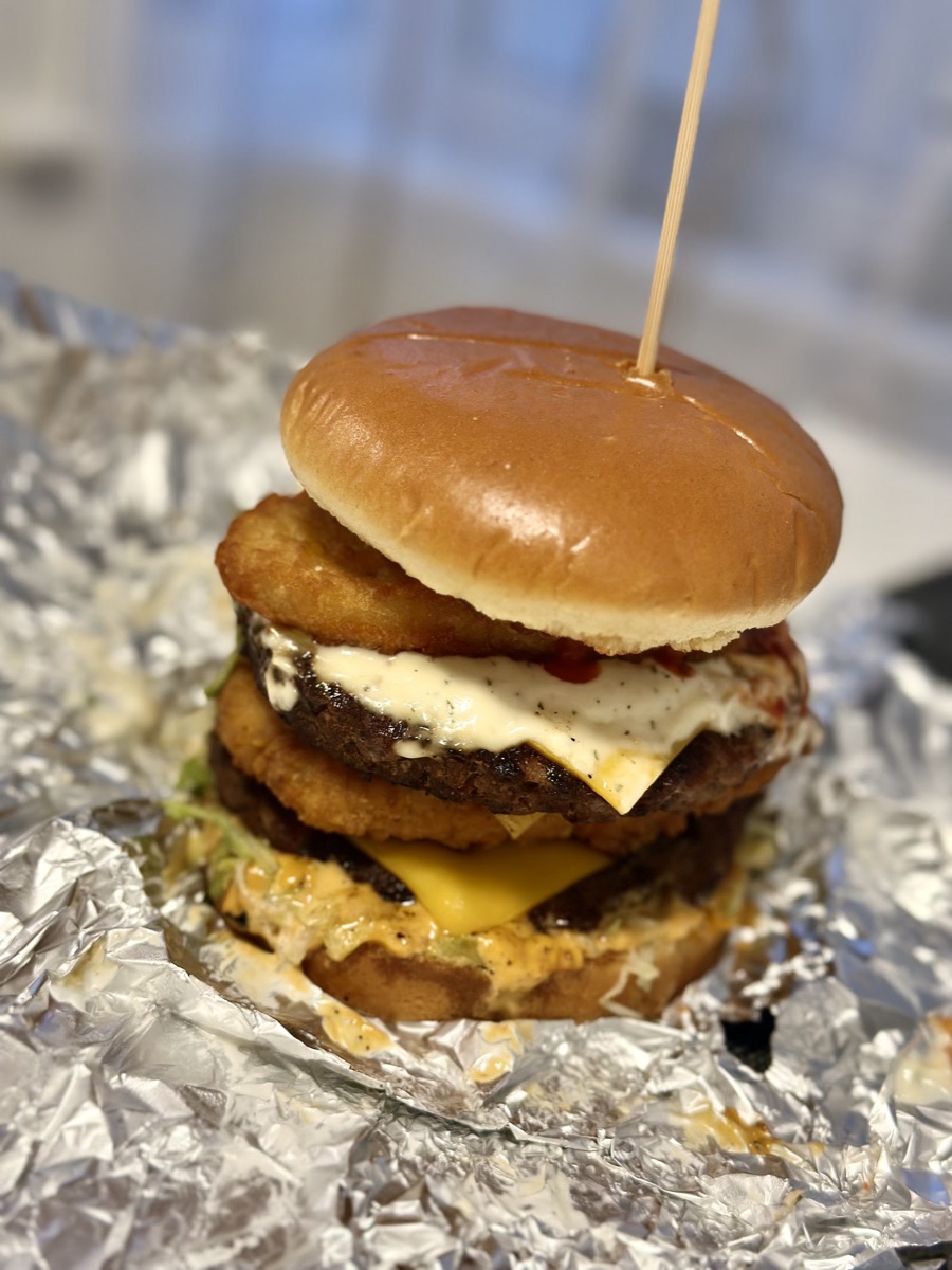 A tall stacked smash burger with hash browns, melted cheese and sauce at Ashes, East Ham