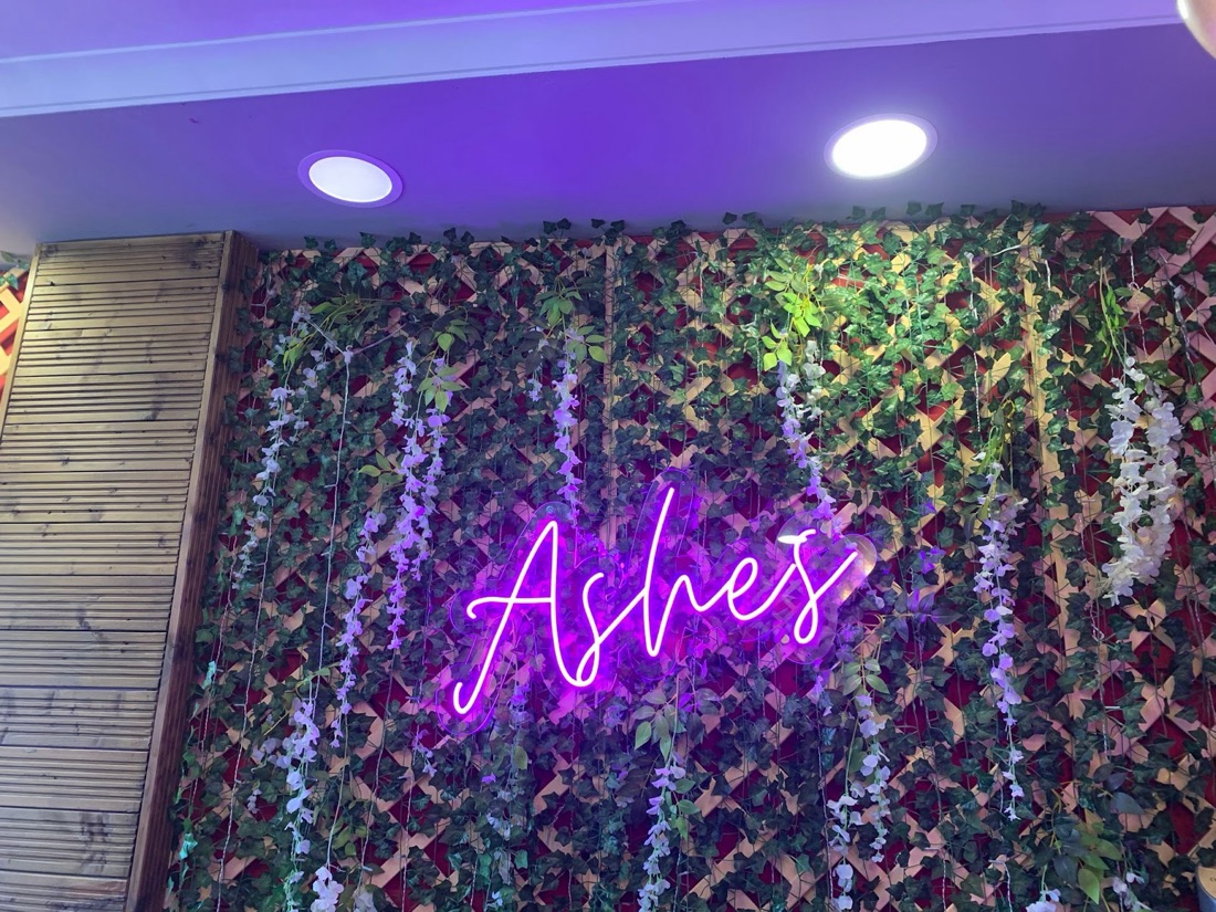 Ashes neon sign on an ivy wall inside the East Ham restaurant